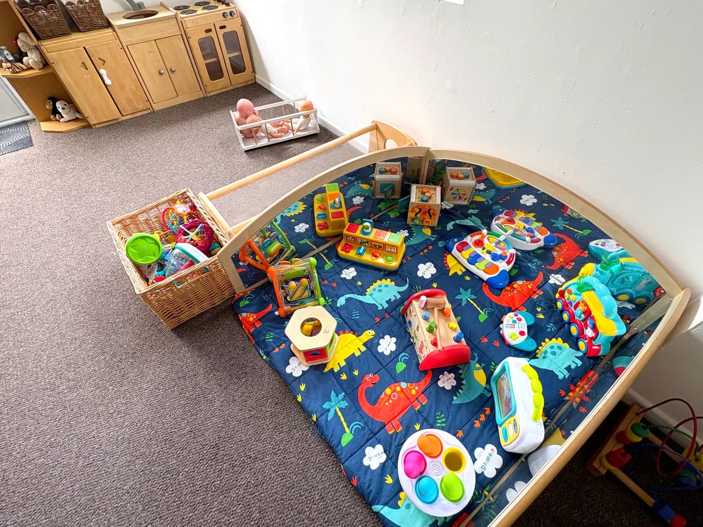 The baby room play area with a mirrored arch, dinosaur play mat and treasure baskets at Blue Nest Montessori Aldershot