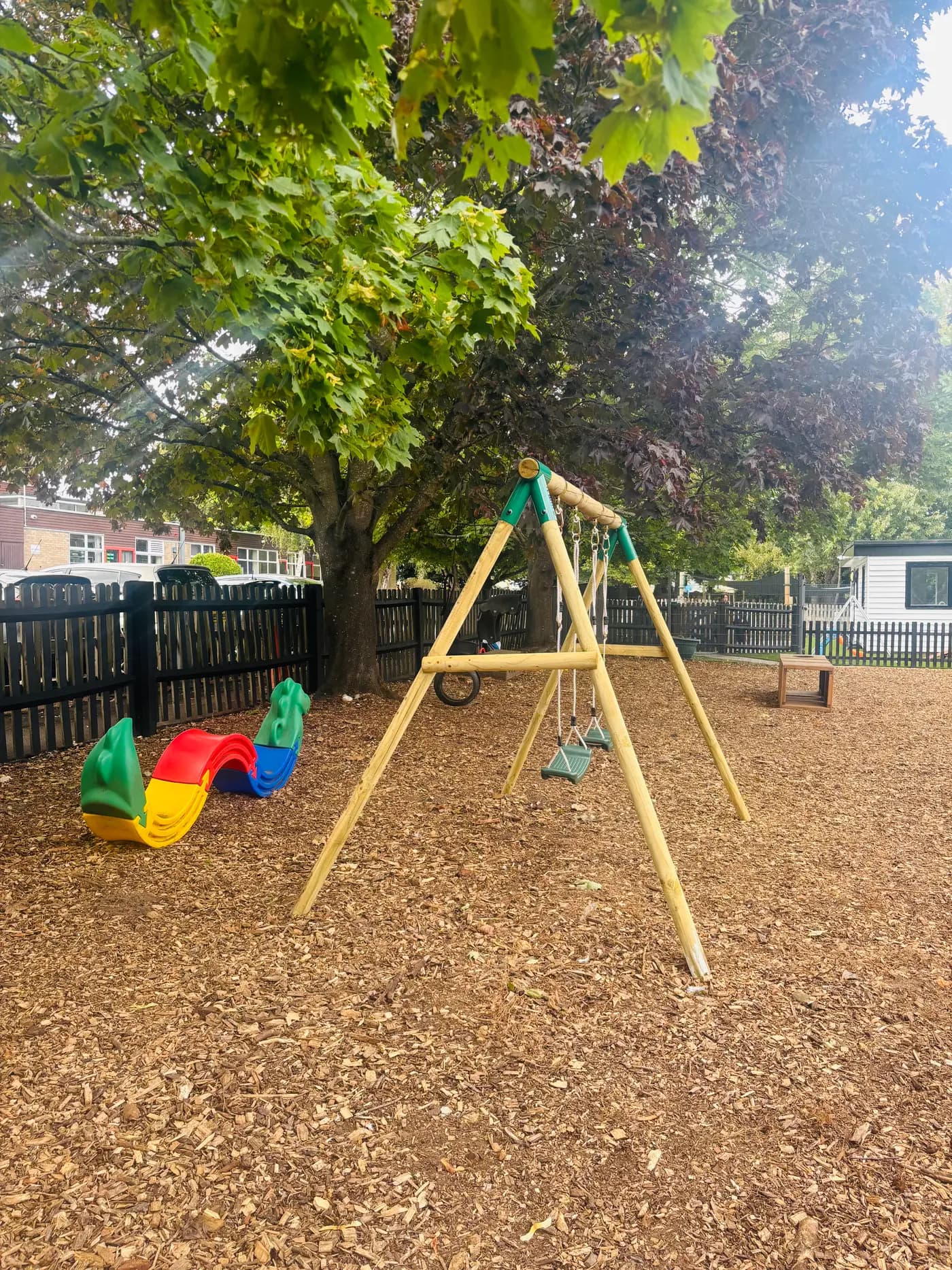 Another view of the swings and tree-shaded playground at Blue Nest Montessori Aldershot