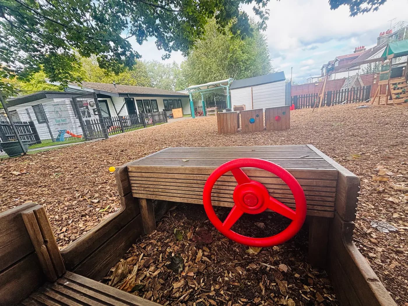 A wooden play car with a bright red steering wheel in the bark-chip yard at Blue Nest Montessori Aldershot