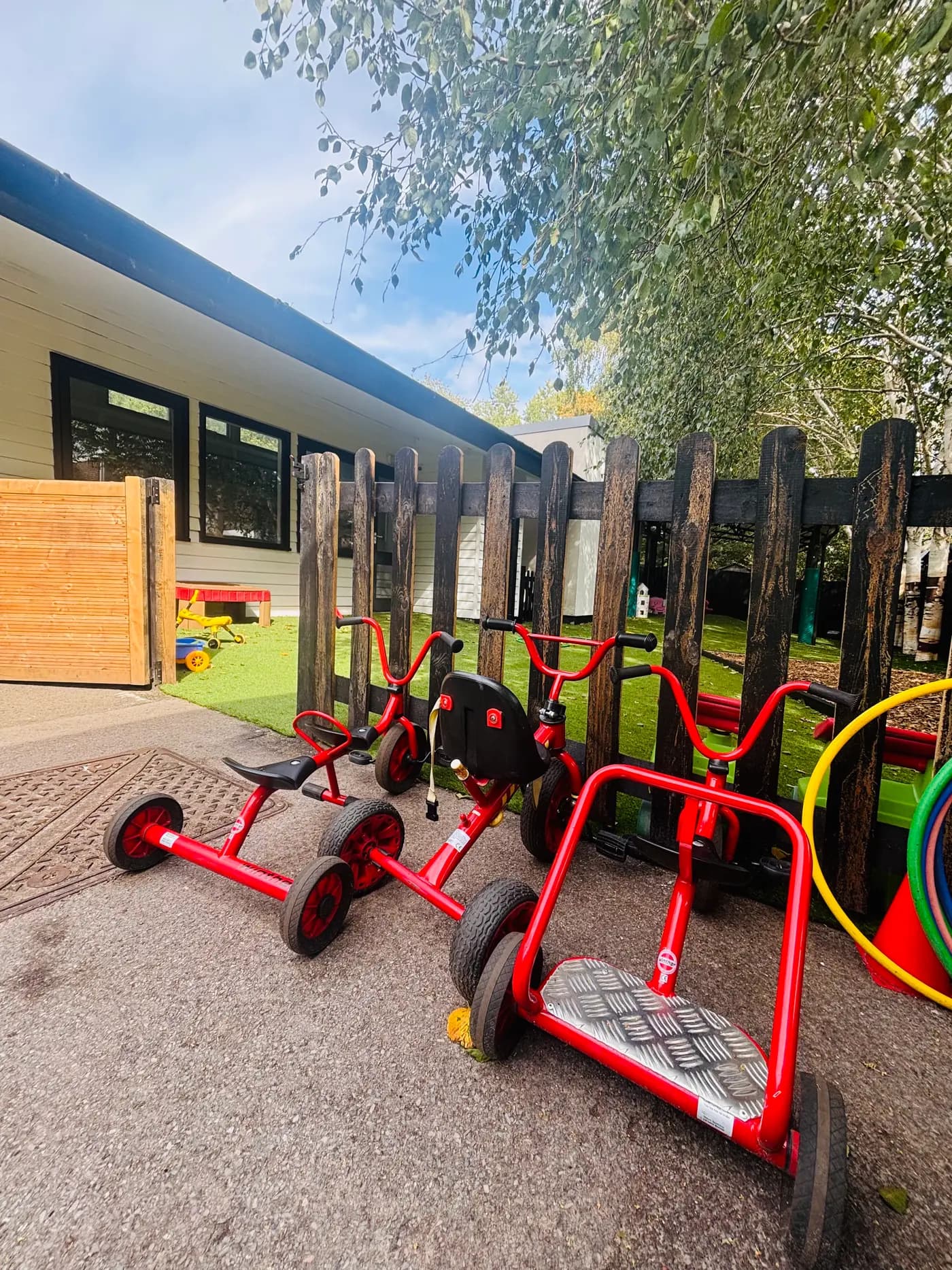 Red trikes and scooters lined up by the garden fence at Blue Nest Montessori Aldershot