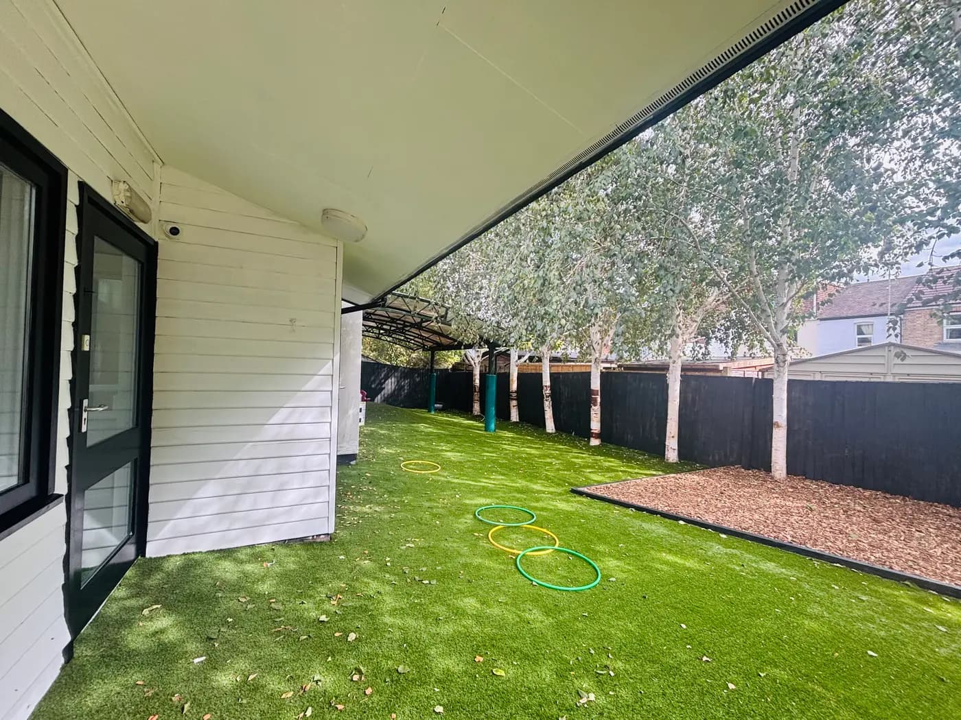 The covered artificial-grass walkway with hoops beneath silver birch trees at Blue Nest Montessori Aldershot