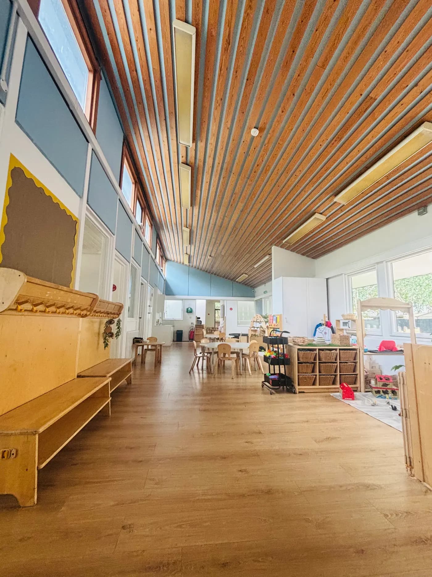 The main hall with its wood-slat ceiling, benches and activity tables at Blue Nest Montessori Aldershot