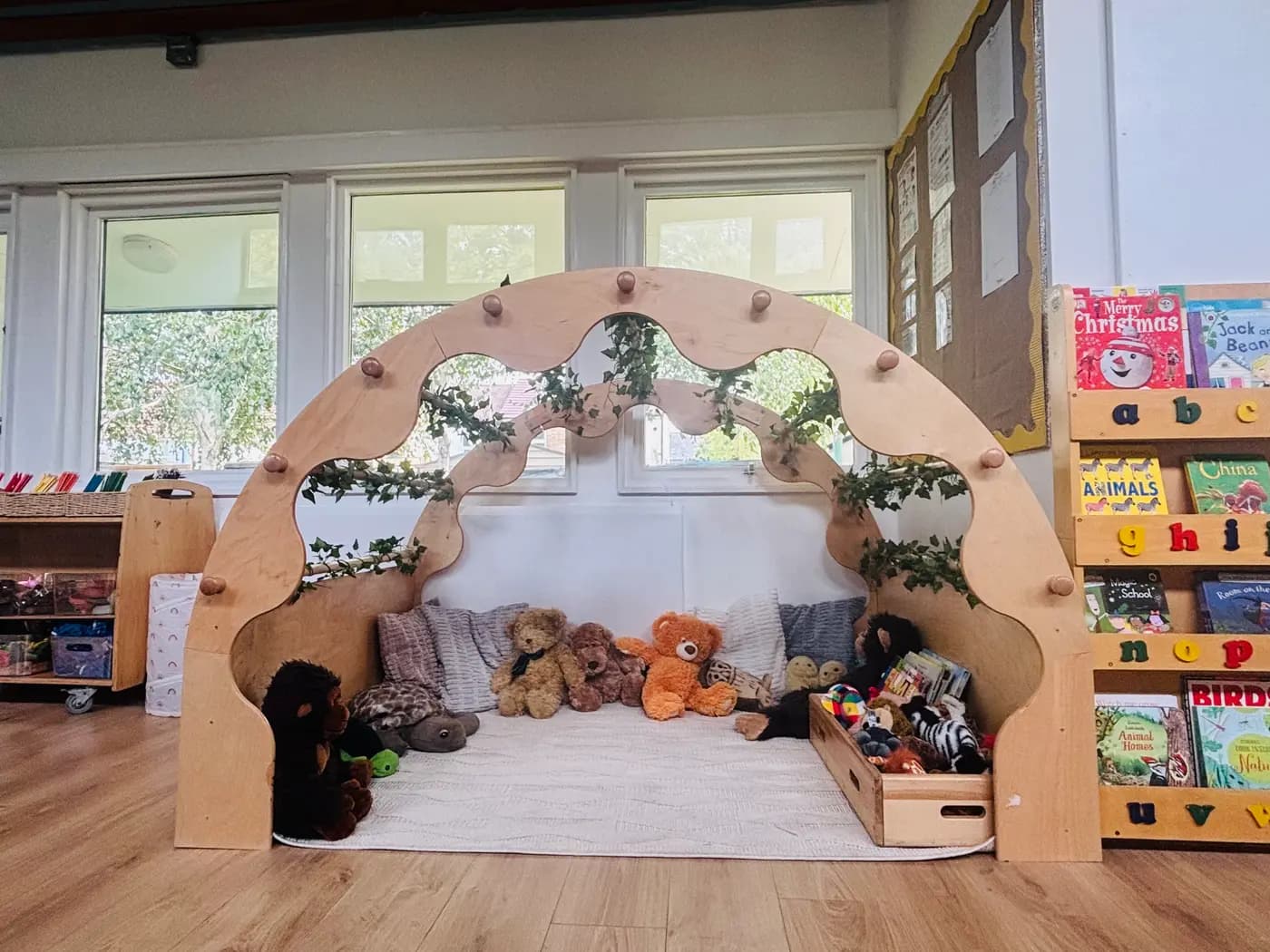 The cosy wooden den filled with teddies beside the alphabet bookshelf at Blue Nest Montessori Aldershot