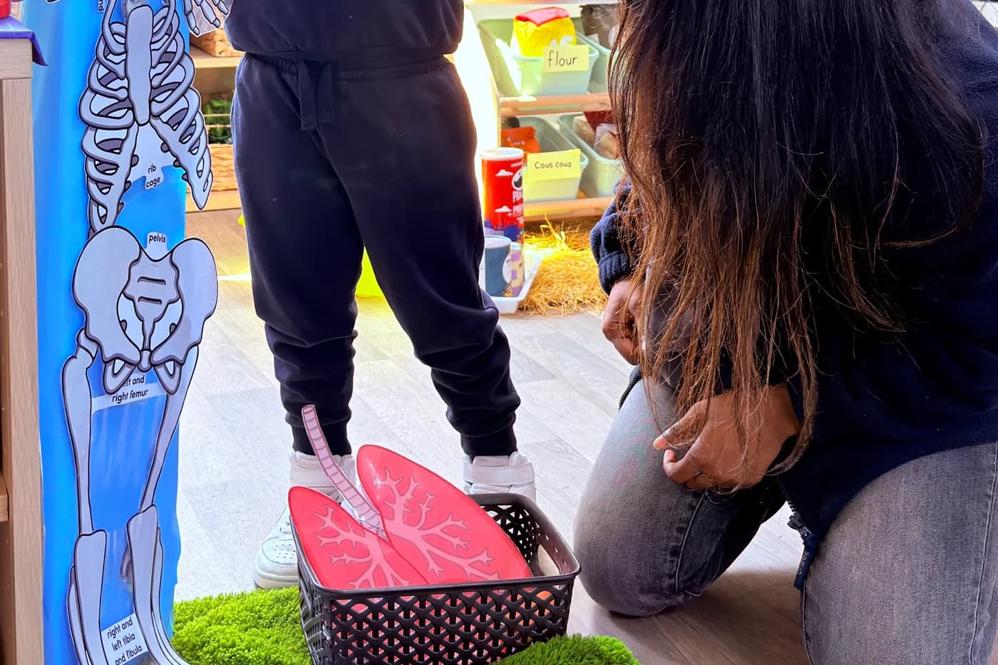 Child reaching up to the skeleton model with a practitioner at Blue Nest Montessori Borehamwood