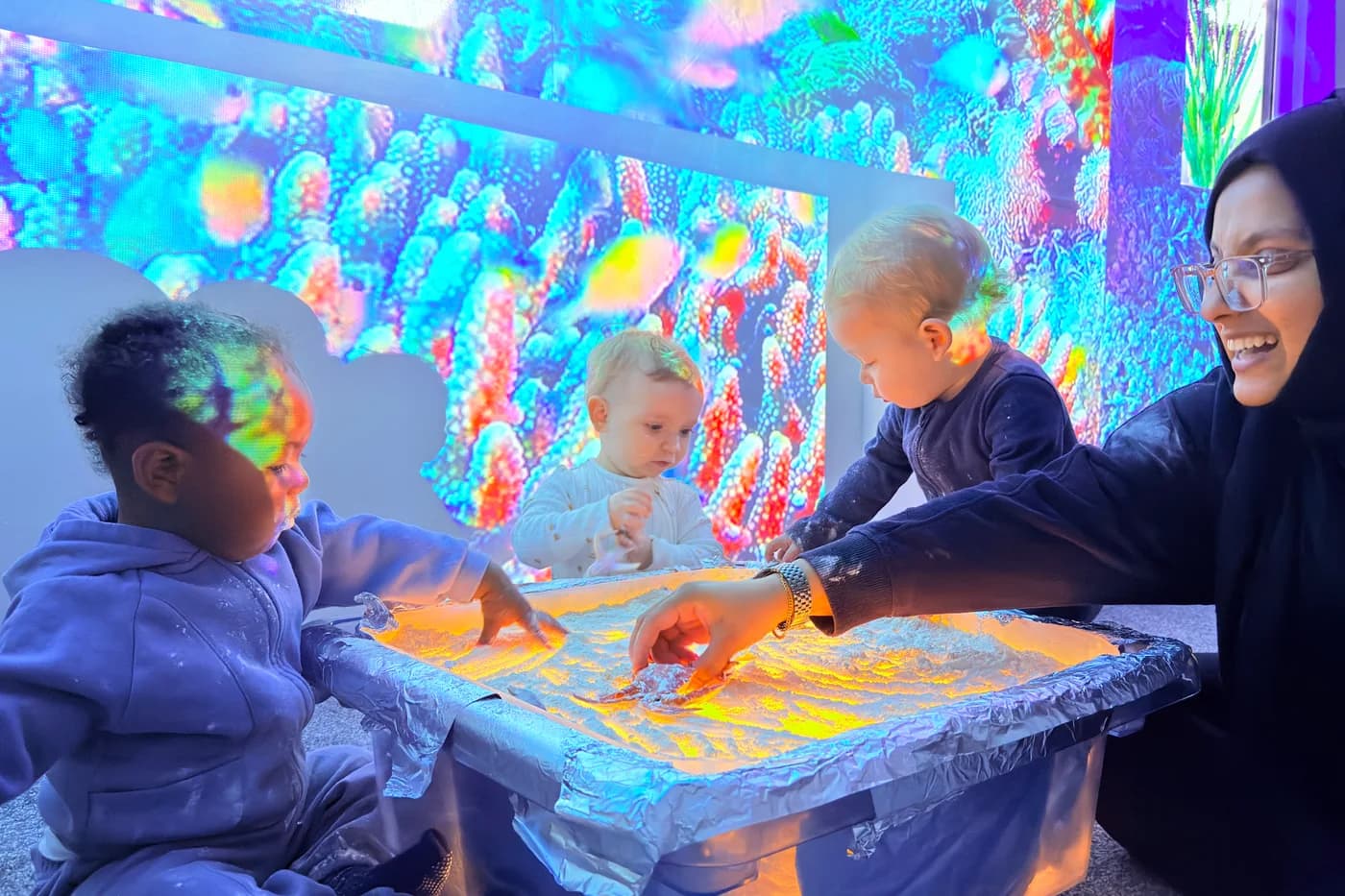 Children gathered at the colourful sensory light table at Blue Nest Montessori Borehamwood