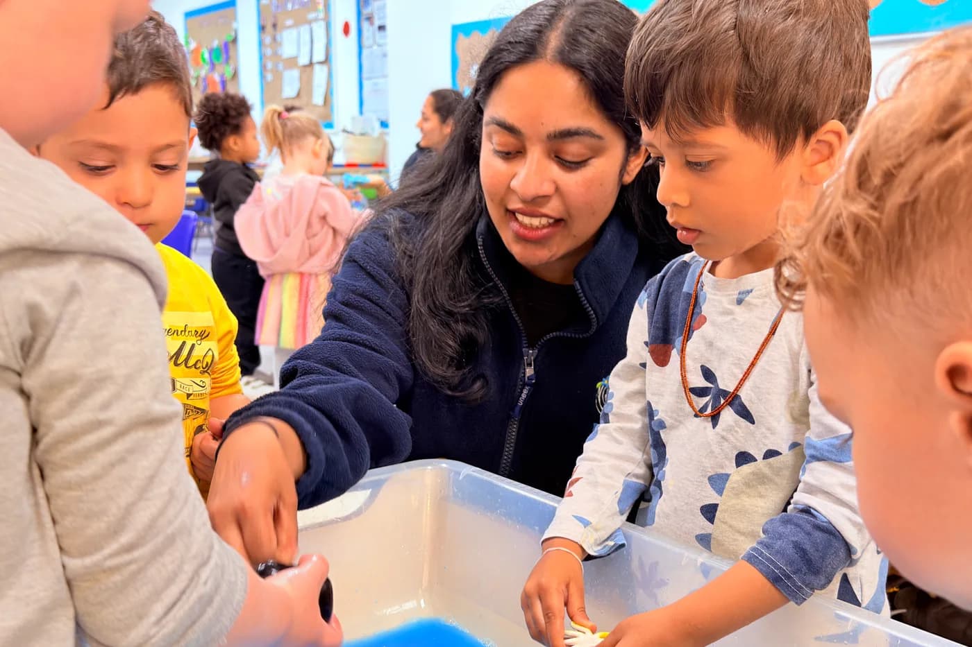 Children and a practitioner at the water exploration tray at Blue Nest Montessori Borehamwood