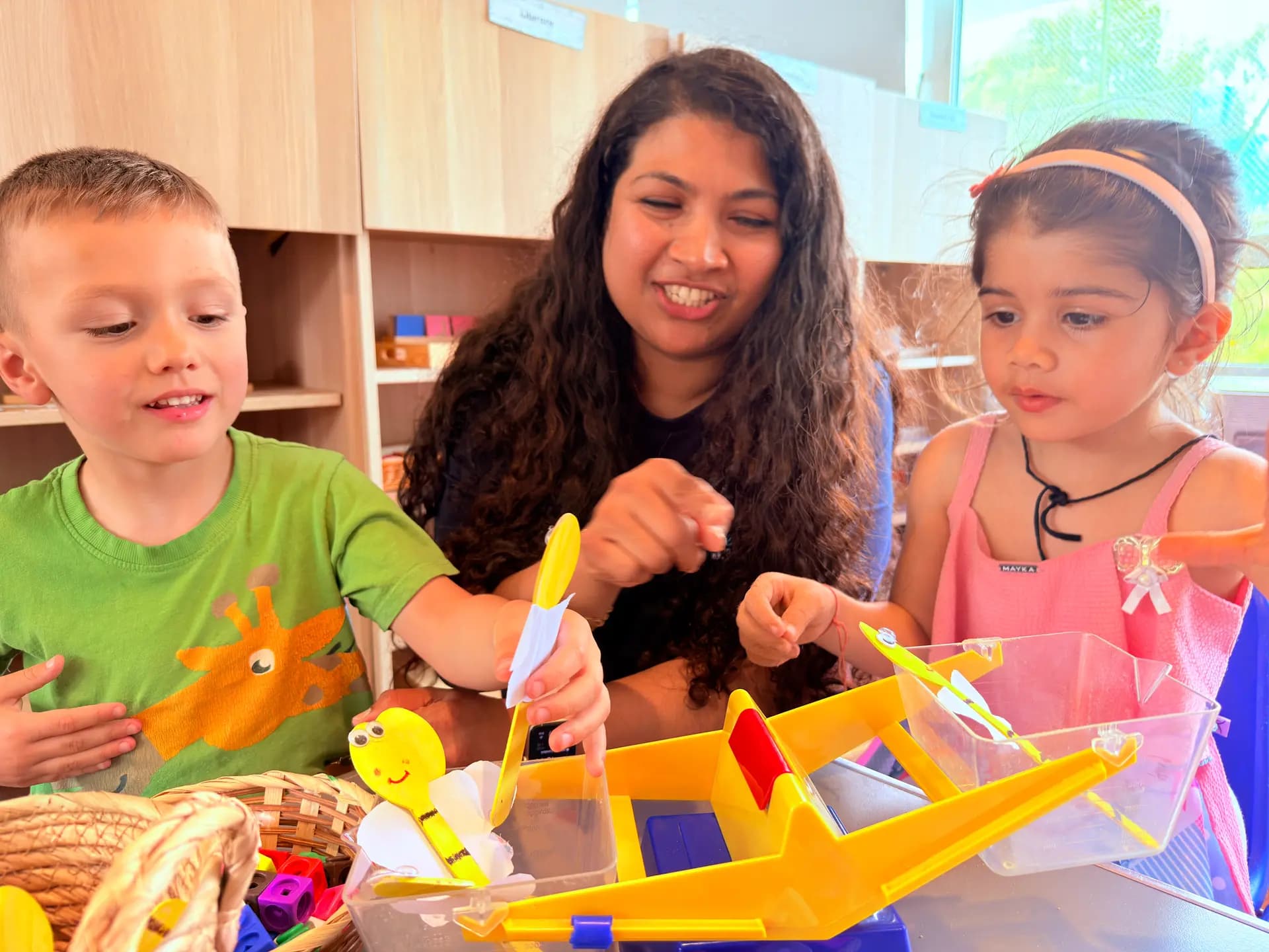An educator engaging two young children in a hands-on activity at Blue Nest Pinner