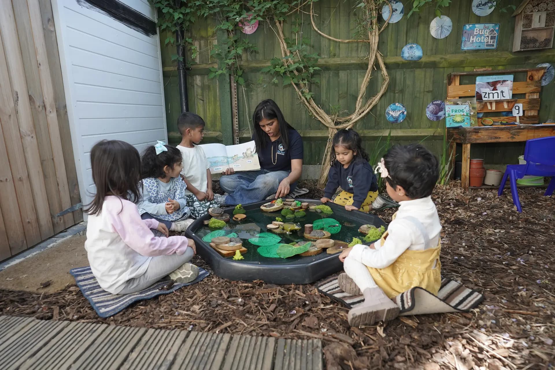 A Blue Nest practitioner sharing a frog story with a group of children around an outdoor water tray