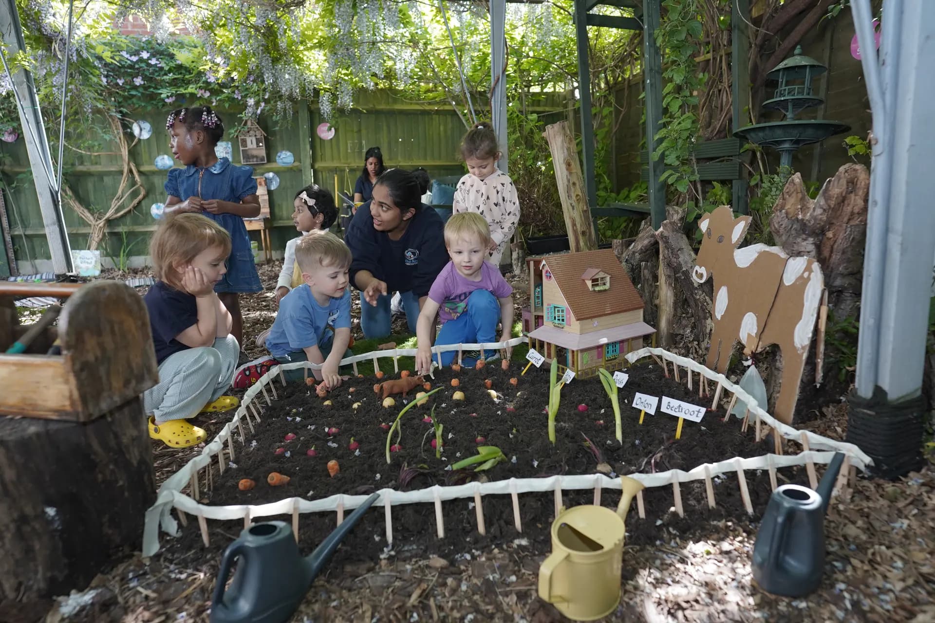 A Blue Nest practitioner supporting a small group of children at the garden planting bed
